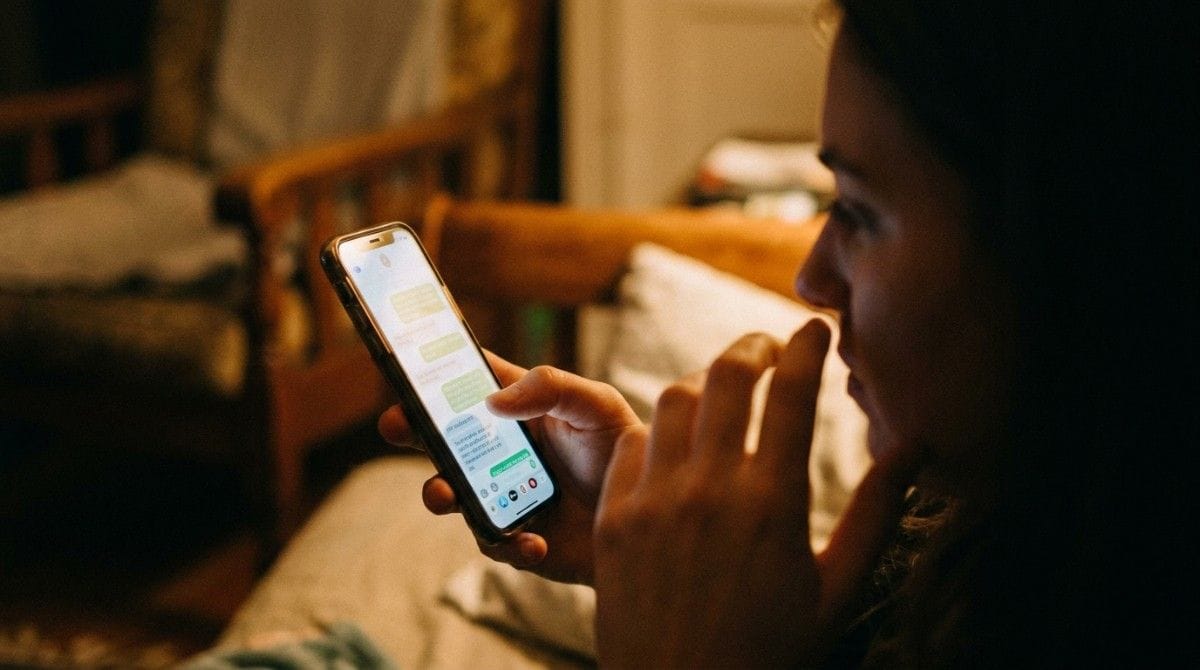 Woman reading and typing text messages on her smartphone while sitting in a dimly lit room at night.