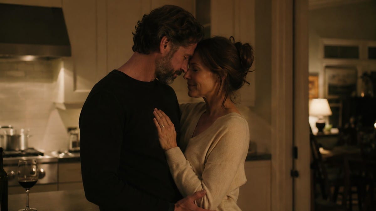 Couple standing close together in a warmly lit kitchen and sharing an affectionate moment.