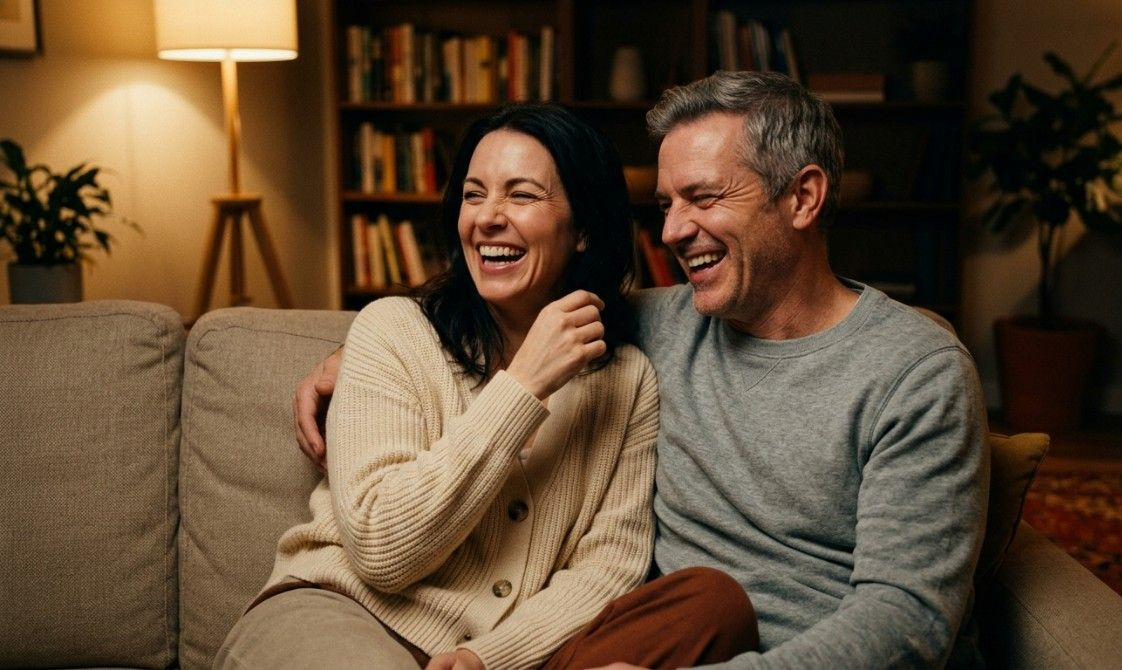 Happy couple laughing together on couch at home during relaxed evening